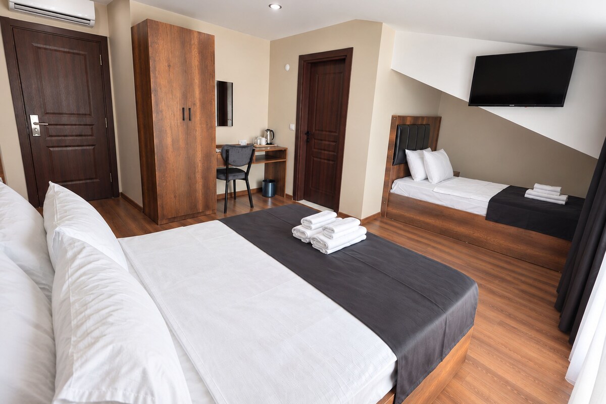 A hotel room with a large bed, a smaller bed, a desk, and a TV mounted on the wall.