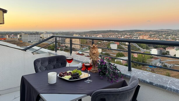 A balcony table with a plate of fruits, two glasses of red wine, and a decorative vase. - BZN AİRPORT HOTEL (Arnavutköy)