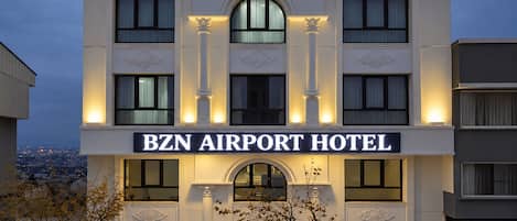 A hotel with a prominent sign reading 'BZN AIRPORT HOTEL' and a red carpet leading to the entrance.
