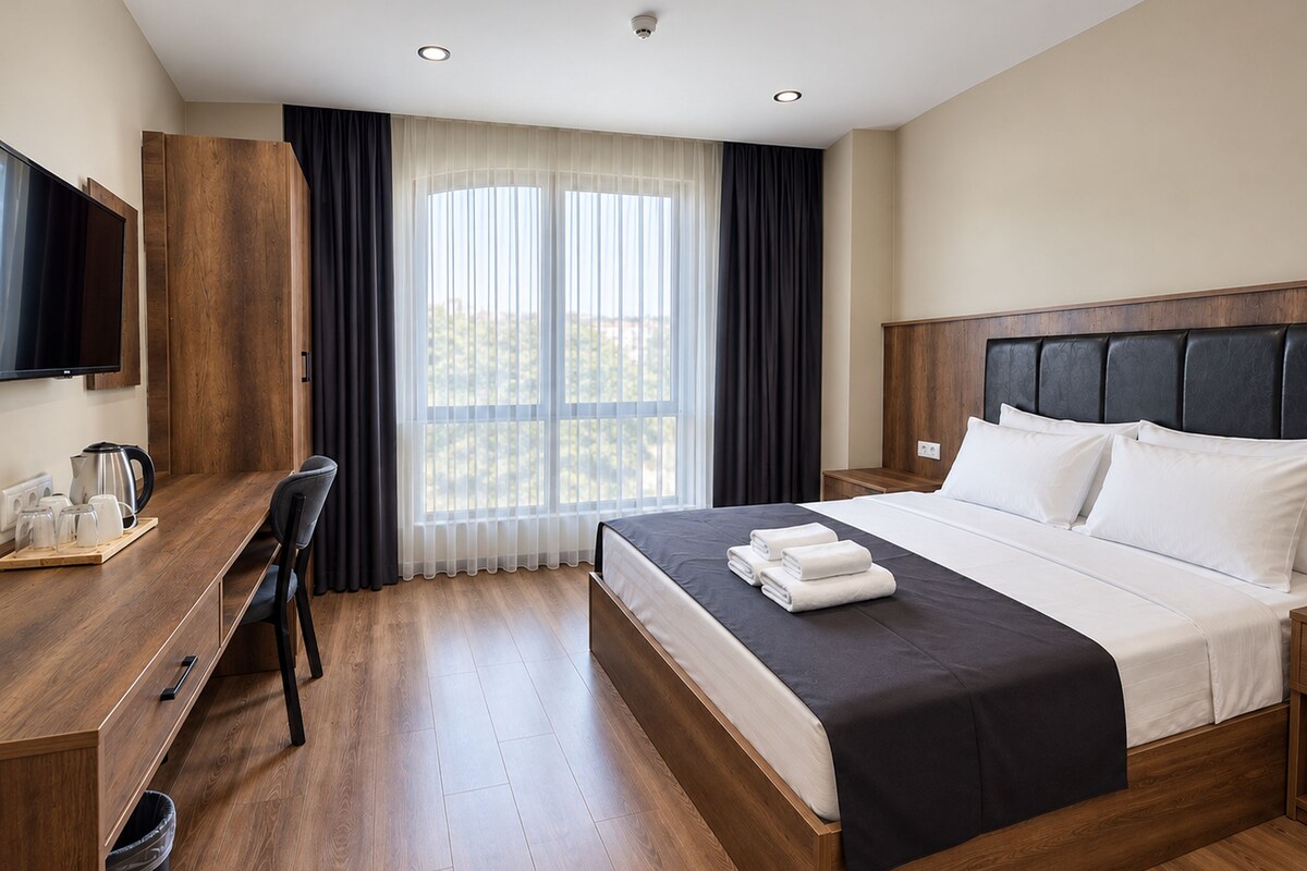 A hotel room with a bed, a desk, a television, and a window with curtains.