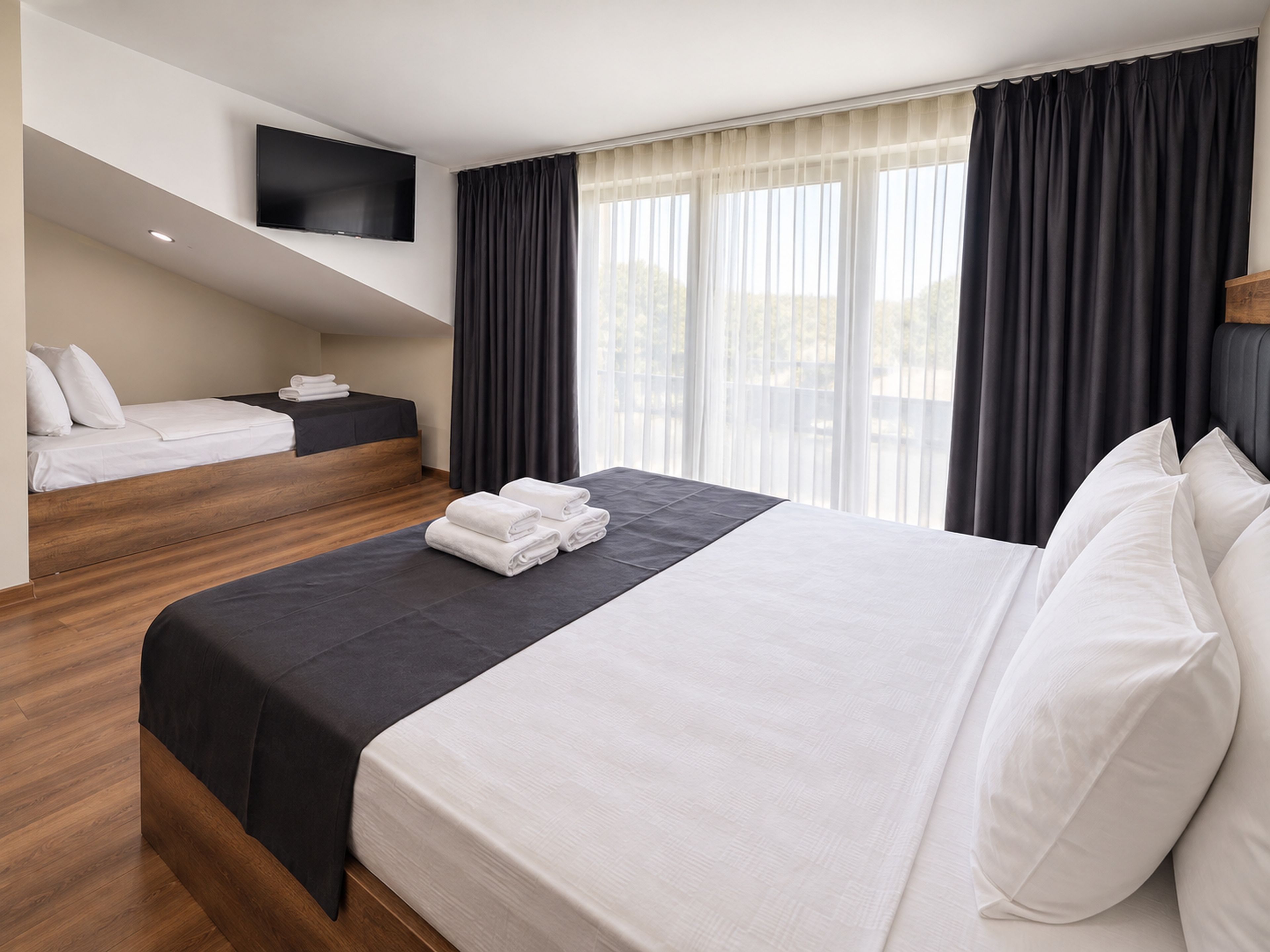 Une chambre d’hôtel avec un grand lit, un lit plus petit, un téléviseur à écran plat fixé au mur et une fenêtre avec des rideaux.
