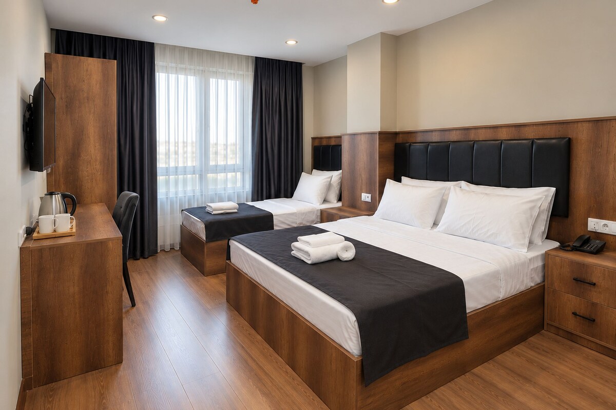 A hotel room with a large bed, a smaller bed, a desk with a chair, a television, and a window with curtains.