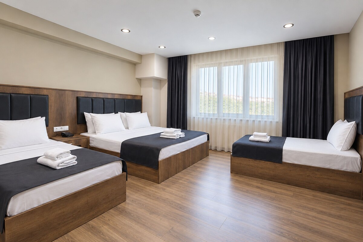 A hotel room with two beds, wooden flooring, and a large window with curtains.