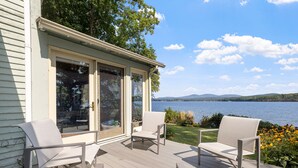 A deck with two chairs and a table, overlooking a lake with mountains in the distance. - Point Comfort On Lake Winnisquam (Sanbornton)