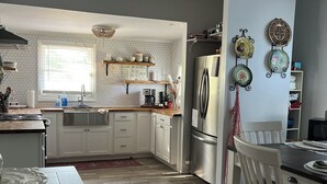 Una cocina moderna con muebles blancos, un refrigerador de acero inoxidable y un comedor con una mesa y sillas de madera.