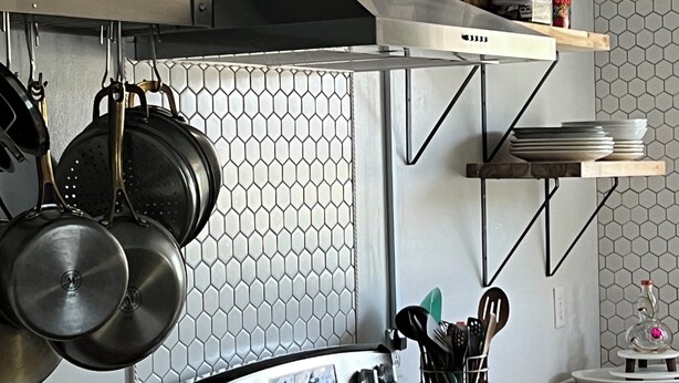 Una cocina moderna con estufa, ollas colgantes y un salpicadero de azulejos hexagonales.