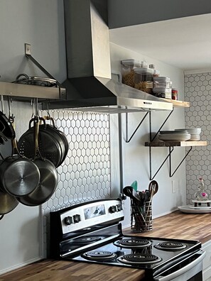Una cocina moderna con estufa, ollas colgantes y un salpicadero de azulejos hexagonales.