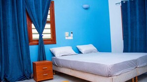 A bedroom with a bed, a wooden nightstand, a small orange rug, and blue curtains.