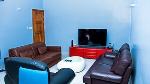 A living room with a brown leather sofa, a black leather chair, a white ottoman, and a red entertainment unit with a TV.