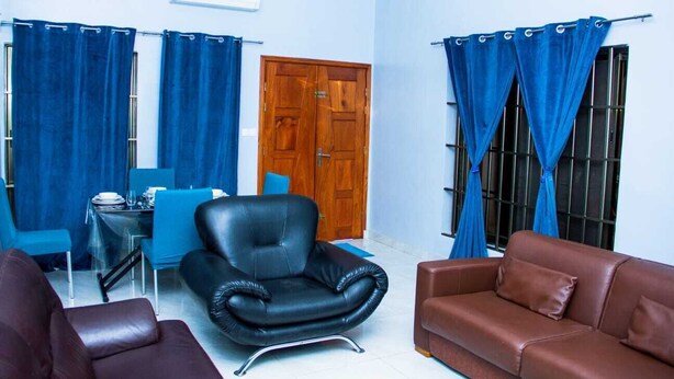 A living room with a brown sofa, a black leather chair, and a blue table set with plates and glasses.