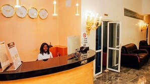 A reception area with a receptionist, a reception desk, a no weapons sign, and a seating area with leather chairs. - Piston Guest Inn (Kano)