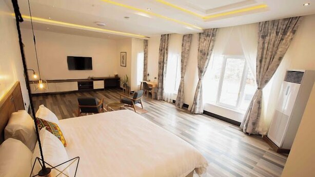 A hotel room with a large bed, a desk, a chair, a TV, and curtains. - Piston Guest Inn (Kano)