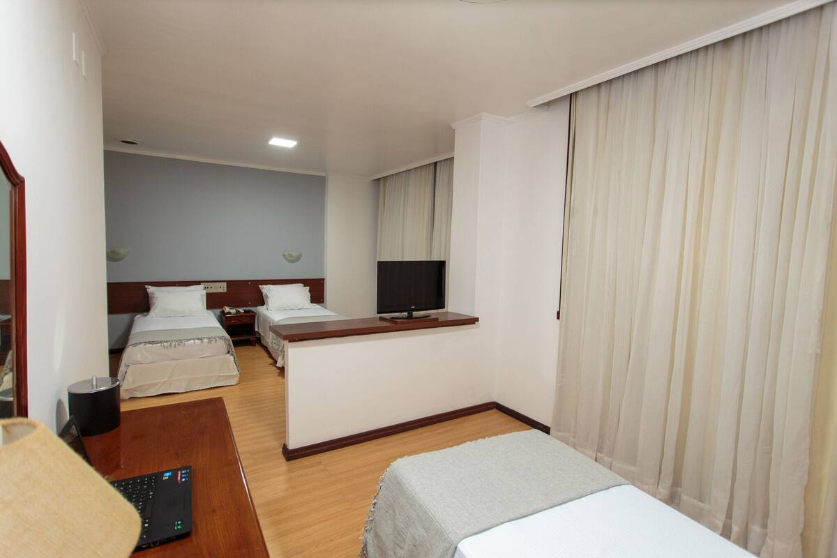 Une chambre d’hôtel avec deux lits, un bureau, une télévision et un rideau.