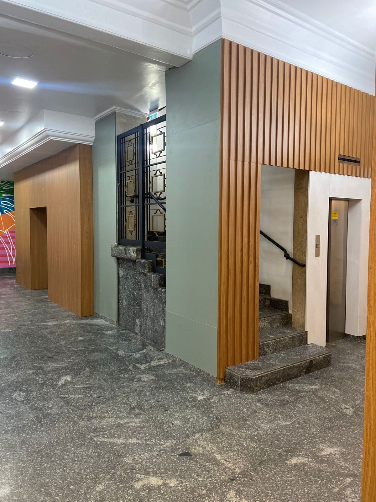 Un interior moderno con piso de mármol, paneles de madera y una escalera que da a un ascensor.