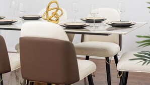 A dining area with a rectangular table set for four, featuring black and gold plates, white chairs, and a gold decorative piece.