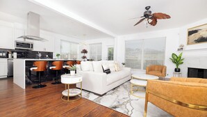A modern living room with a white sofa, a round coffee table, and a yellow armchair. There is a kitchen area with a black countertop and white cabinets.