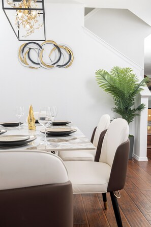 Uma área de refeições com uma mesa de mármore, cadeiras brancas e castanhas, e um vaso com planta.
