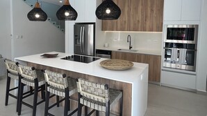 A modern kitchen with a central island, stainless steel appliances, and a wooden accent wall. - Casa Las Flores - Tropical Luxury Retreat Pinilla (Pinilla)