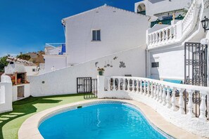 Un edificio blanco con piscina, un pequeño jardín y un balcón con barandilla blanca.