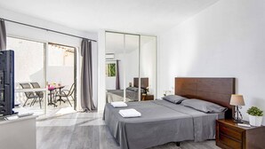 Ein modernes Schlafzimmer mit einem großen Bett, einem Nachttisch, einem Fernseher und einem Balkon mit Tisch und Stühlen.