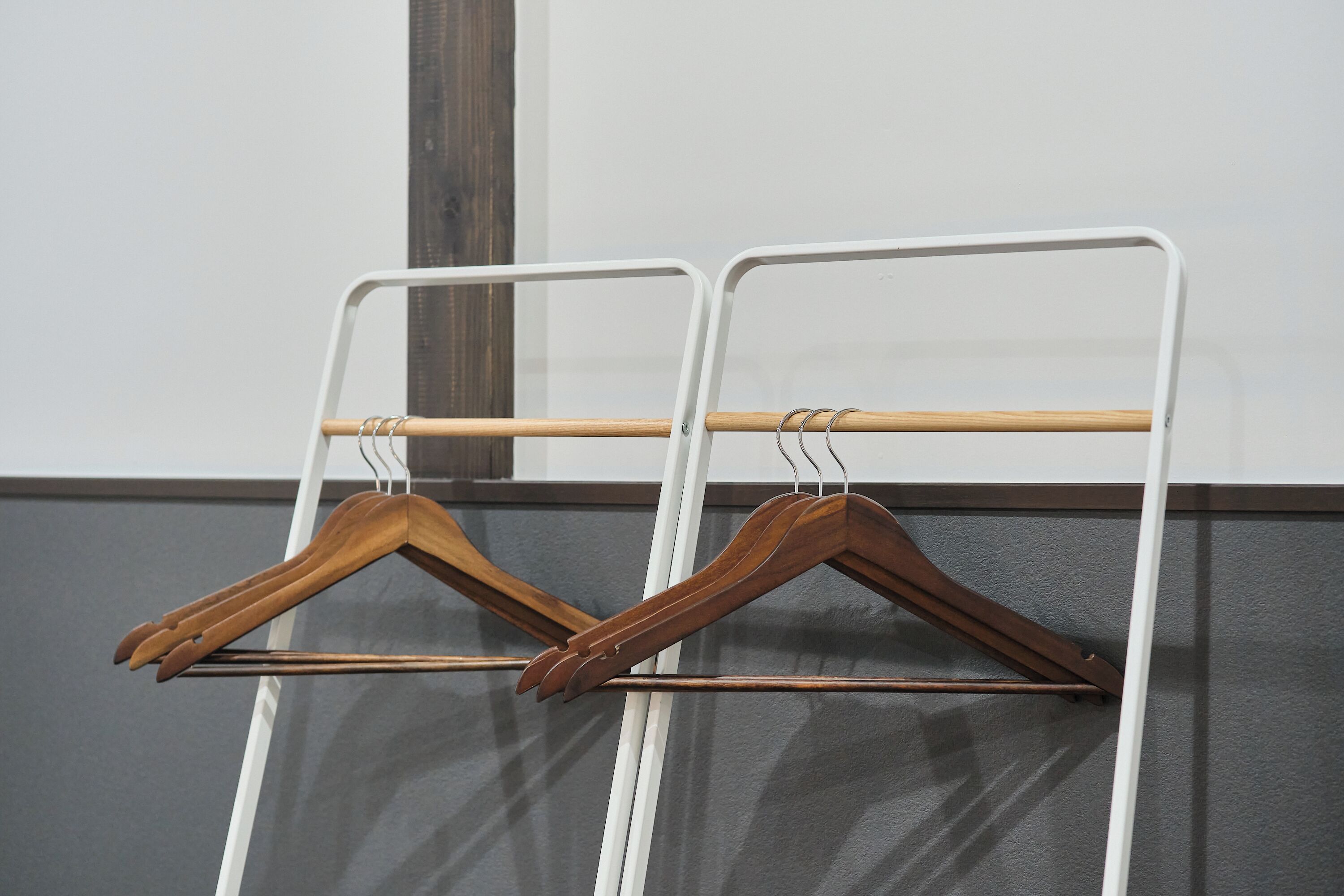 A white metal rack with wooden hangers against a grey wall.