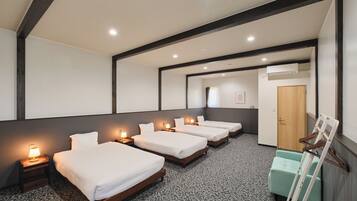 Habitación de hotel con cuatro camas individuales, una puerta de madera, un pequeño espacio de descanso y una alfombra estampada.
