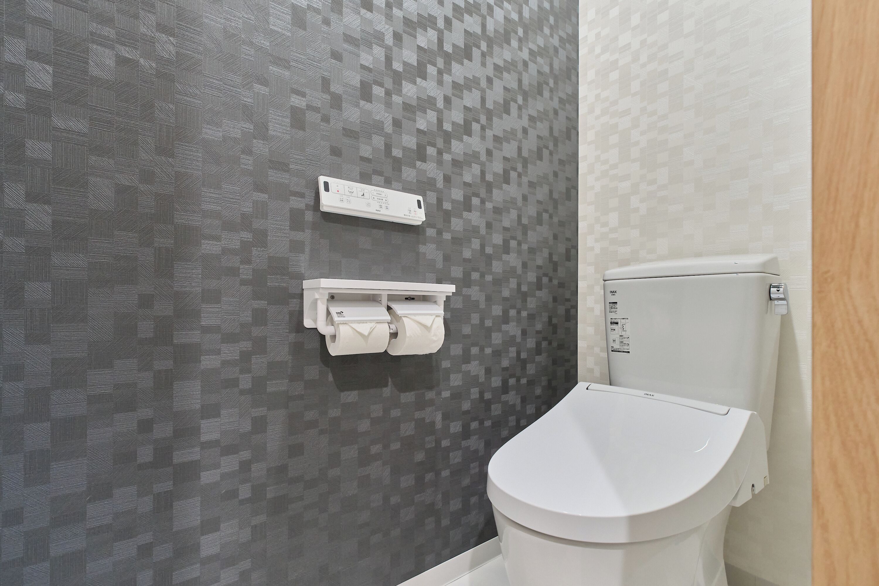 A bathroom with a toilet, a paper towel dispenser, and a wall-mounted control panel.