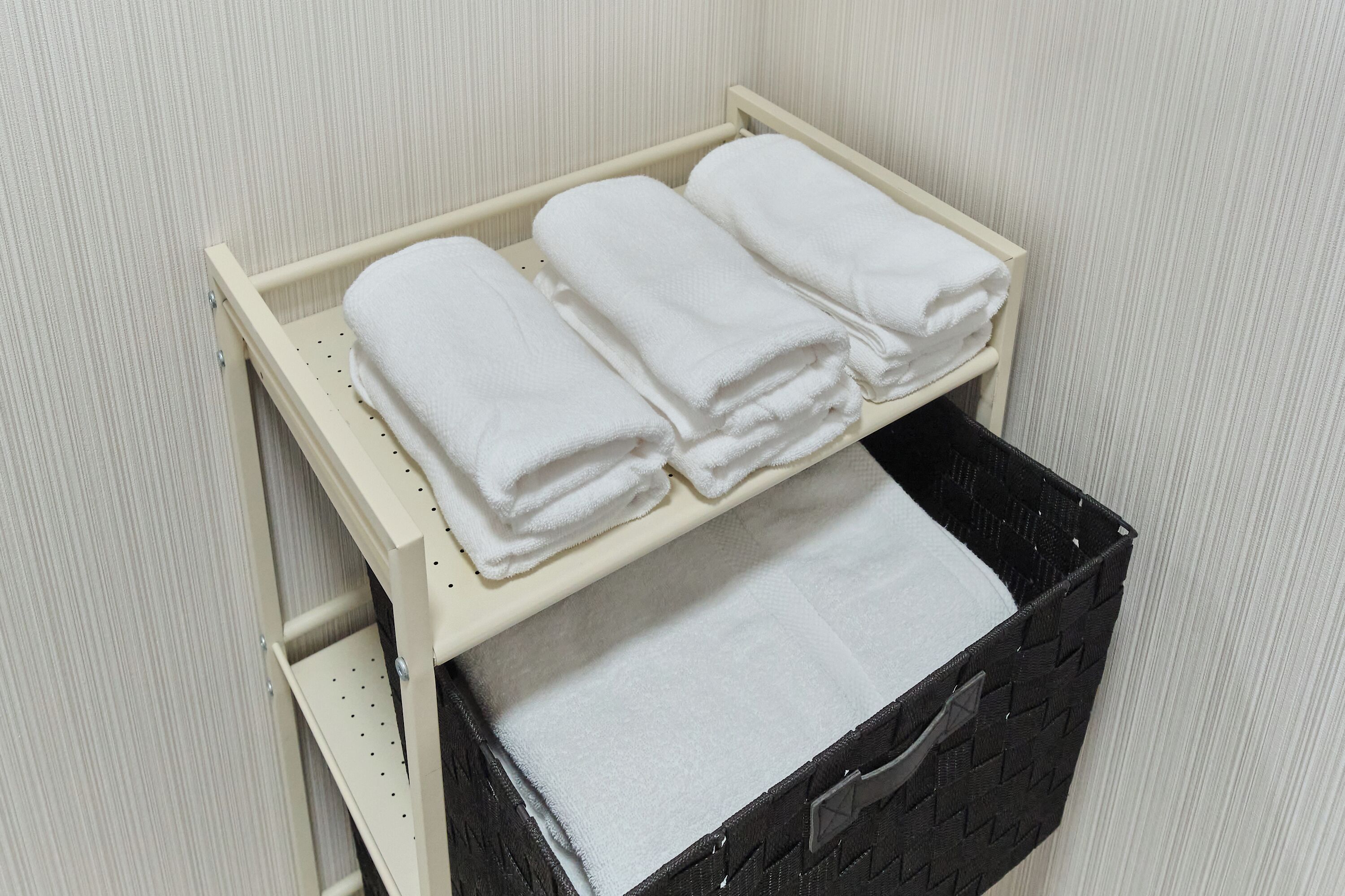 A storage unit with three neatly folded white towels and a black basket.