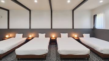 A hotel room with four single beds, each with a bedside table and lamp, and a large window with curtains.