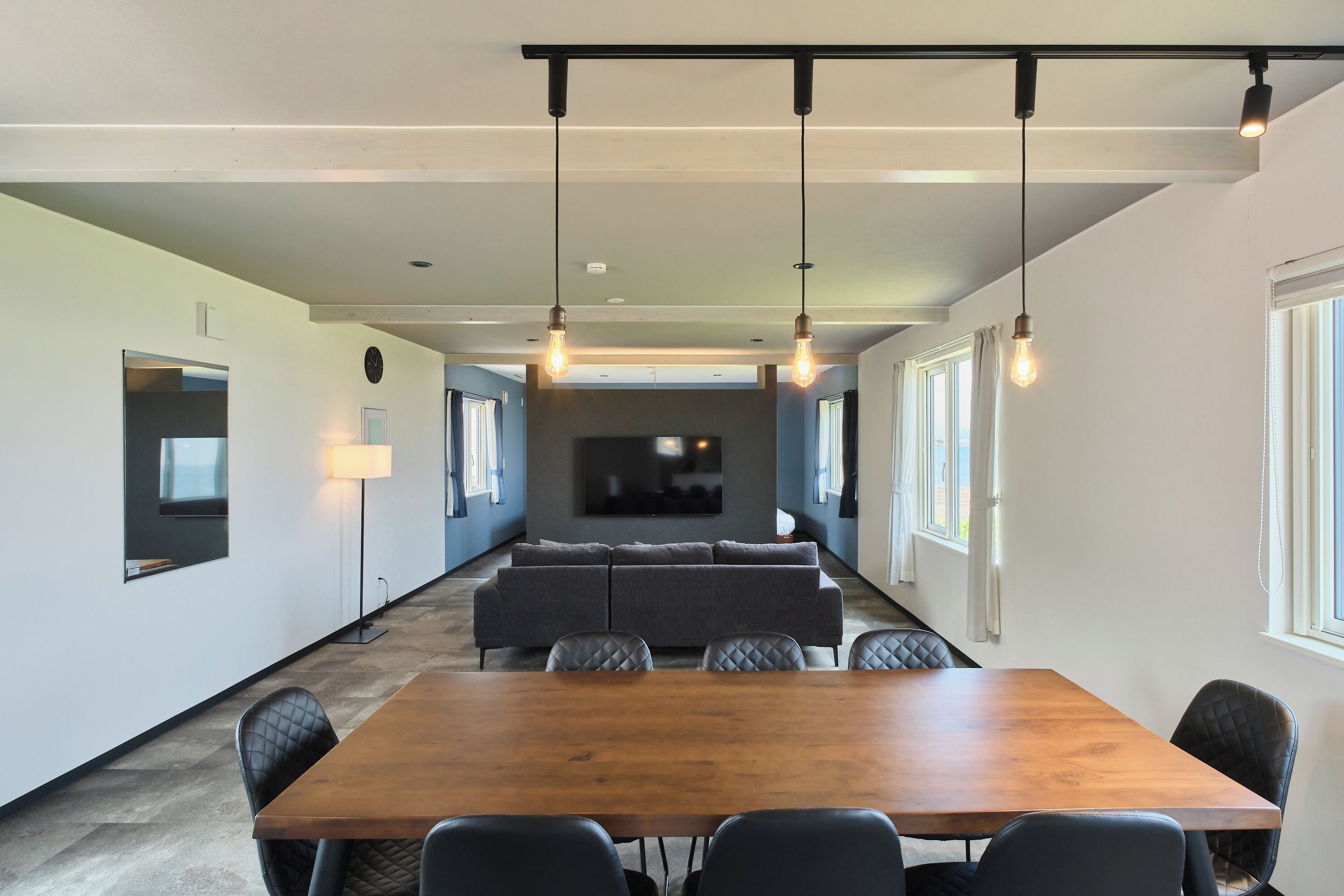 A modern conference room with a long table, multiple chairs, a sofa, and pendant lighting.