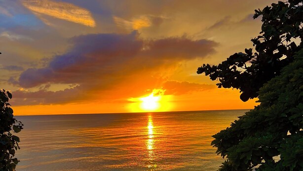 Ein Strandbild mit Sonnenuntergang, Menschen, die spazieren gehen, und einer Treppe, die zum Strand hinabführt.