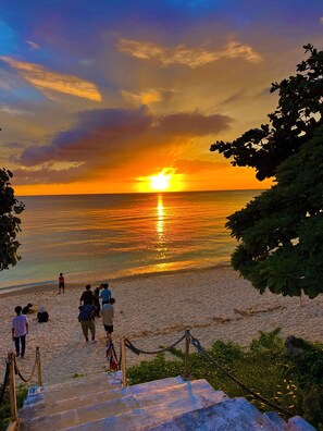 A beach scene with a sunset, people walking, and a staircase leading down to the beach. - Charming 3-bedroom house with AC and WiFi in serene Okinawa (nakagami)