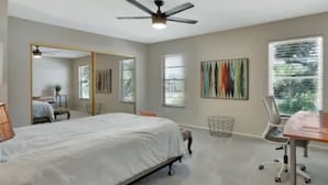 Un dormitorio con cama, escritorio, silla, ventilador de techo y ventana.