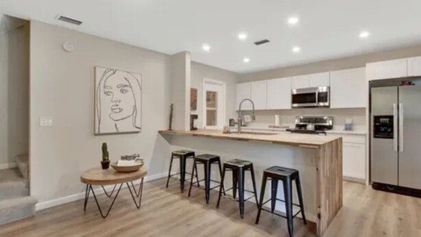 Una cocina moderna con una isla de madera, taburetes de bar y un refrigerador.