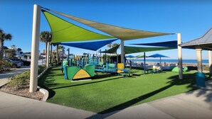 Un parque infantil con estructuras para escalar y zonas de estar a la sombra.