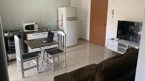 A compact living space with a kitchenette, a dining area with a table and chairs, a sofa, and a TV. - Studio Space SM Araguaia (Vila Galvão Guarulhos)