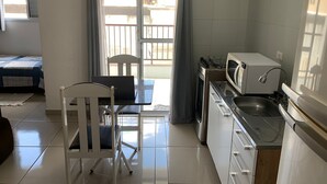 A compact kitchen with a microwave, stove, and sink. There is a dining area with a chair and table, and a bed in the adjacent room. - Studio Space SM Araguaia (Vila Galvão Guarulhos)