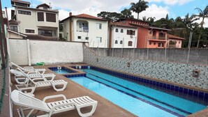 A swimming pool with lounge chairs, a tiled wall, and residential buildings in the background. - Studio Space SM Araguaia (Vila Galvão Guarulhos)