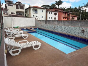 Una piscina con sillas de descanso, una pared de azulejos y edificios residenciales al fondo.