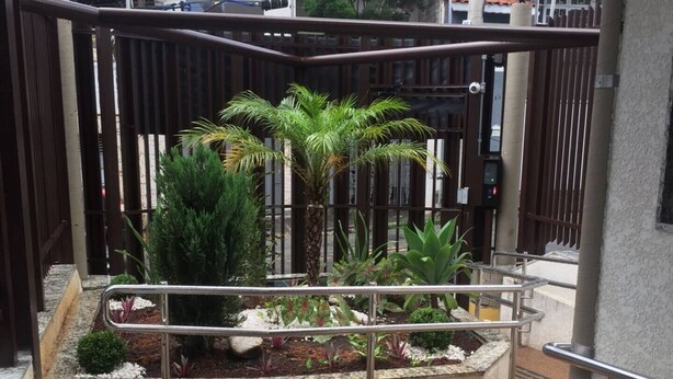 A small outdoor garden area with a concrete planter, palm trees, and a metal railing. - Studio Space SM Araguaia (Vila Galvão Guarulhos)