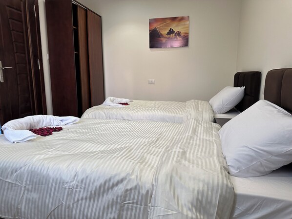 A hotel room with two beds, a painting on the wall, and a wooden wardrobe. - Sun 3 Pyramids Inn (Giza)