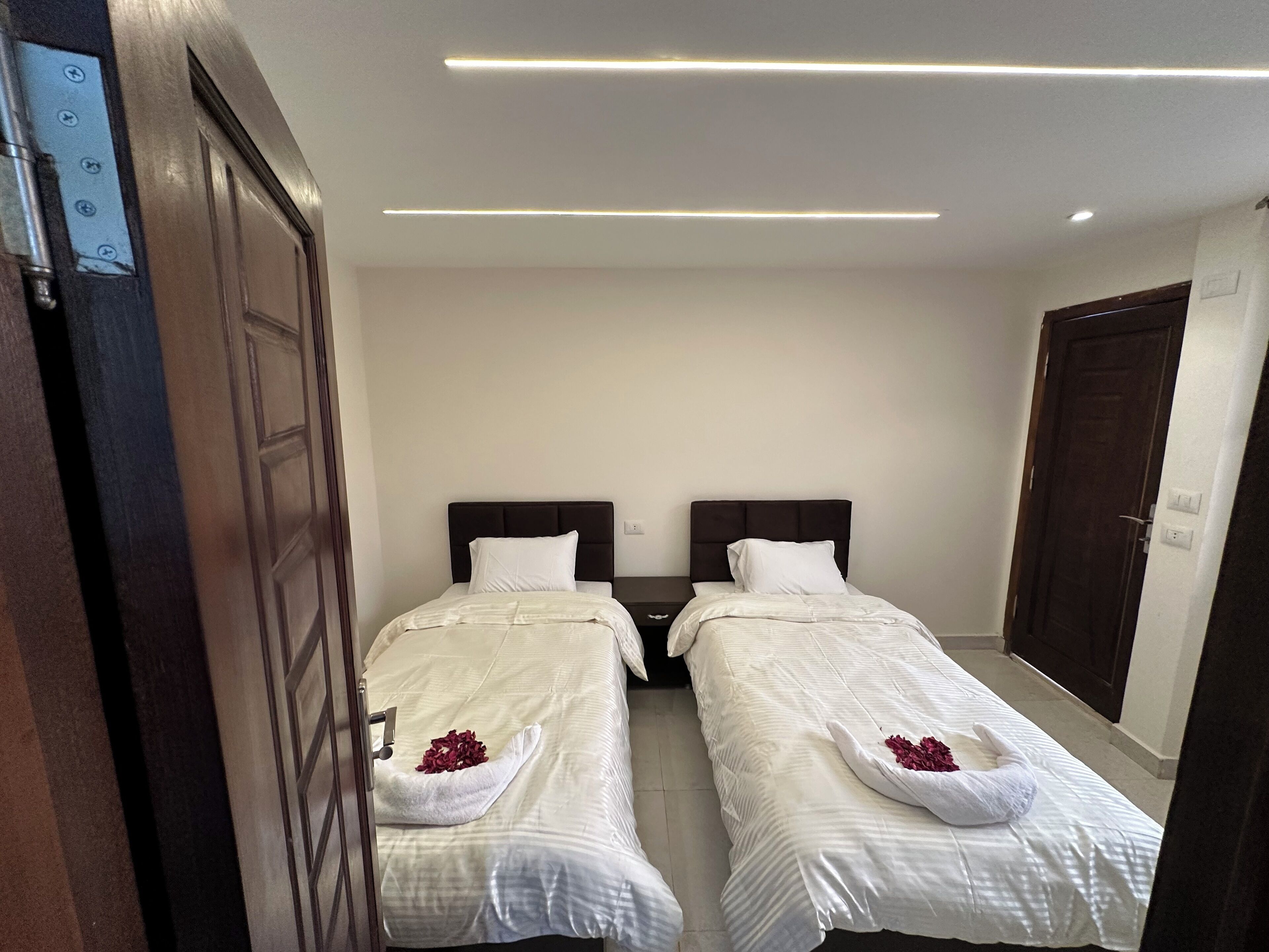 Une chambre d’hôtel avec deux lits simples, une porte en bois et un luminaire moderne au plafond.