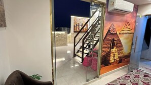 Un hall d’hôtel avec un tapis à motifs, un fauteuil marron, une cloison en verre ornée d’une affiche et un escalier.