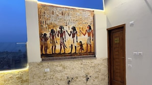 Un mur orné d’une fresque de l’Égypte ancienne, une porte en bois et un sol carrelé.
