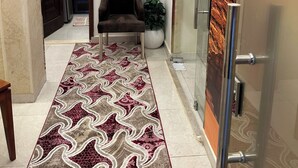 Un hall d’hôtel avec un tapis à motifs, un fauteuil, une plante en pot et une porte en verre.