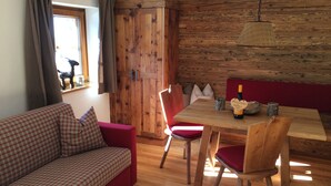 A cozy room with a wooden wall, a checkered sofa, a dining table with chairs, and a hanging light fixture.