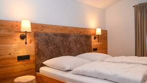 A wooden bed with white bedding, two wall-mounted lamps, and a wooden nightstand.