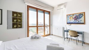 A hotel room with a large bed, a desk, a chair, a window with a view, and artwork on the wall. - Bright apt. Duomo overview (Milano)
