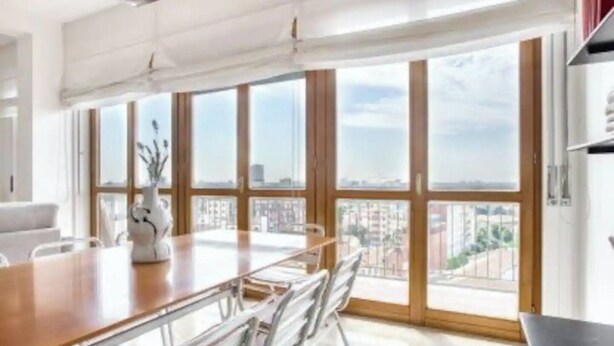 A modern kitchen with a large dining table, white cabinets, and large windows offering a city view. - Bright apt. Duomo overview (Milano)