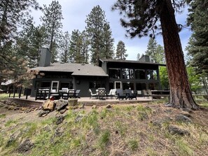A modern building with a patio area, outdoor seating, and a large tree in the foreground. - Rockrose- Perfect multifamily home (Sisters)